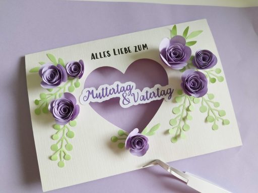 Mutter- & Vatertagskarte in einem Mutter- & Vatertagskarte mit diesem Text, ausgeschnittenen Herz in der Mitte udn mit 3D Papierrosen in flieder und grünen Zweigen