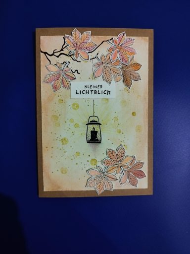 Karte Kleiner Lichtblick Herbstkarte mit bunten Blättern auf einem Zweig und einer Hängelampe mit Lichtstrahlen. Dazu der Text: Kleiner Lichtblick