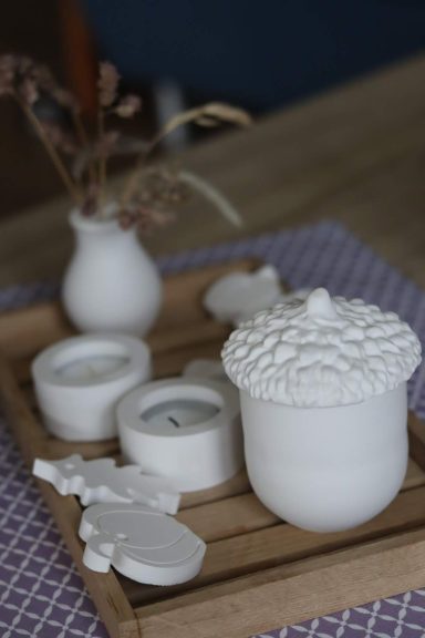 Herbstdeko Weiße gegossene Dekoelemente auf Holztablett: Vase mit Trockenblumen, zwei Teelichthalter, Pilzen und Dose in Form einer Eichel